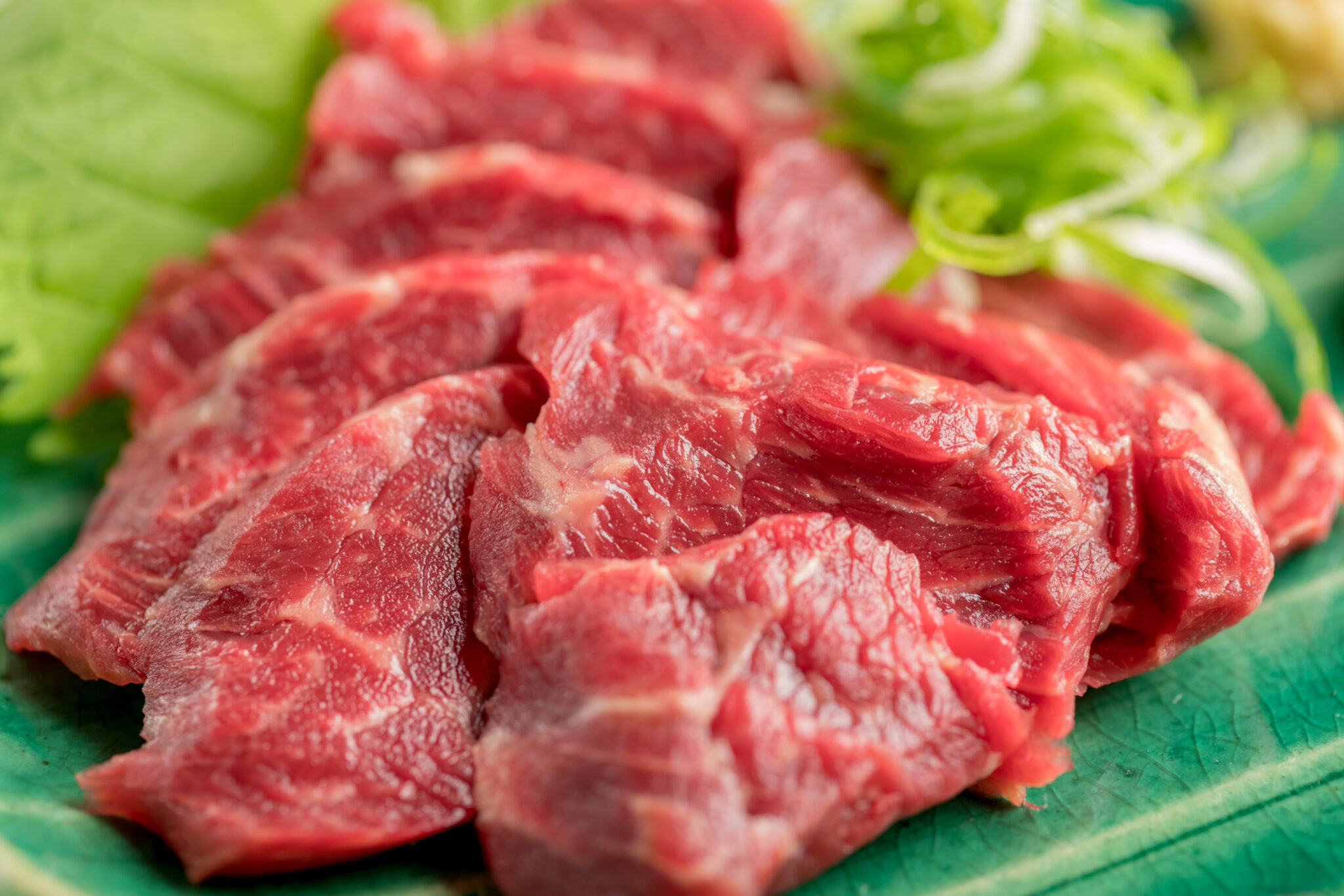 緑の皿に白髪ねぎと大葉を添えて盛り付けた、鮮やかな赤身の馬刺し