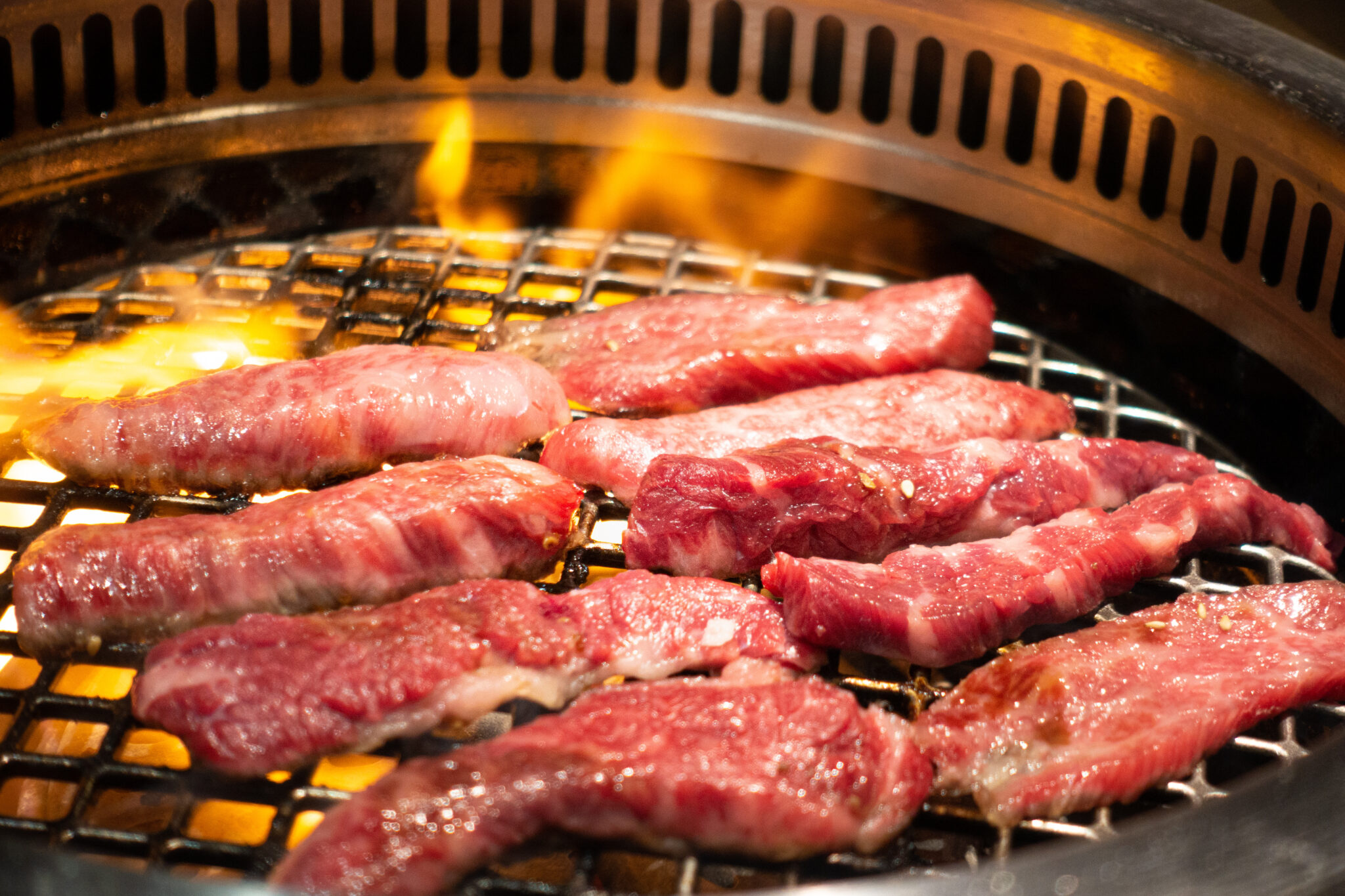 焼肉店の丸網の上で、炎を上げながら焼かれるタレ付きの牛肉の切り身