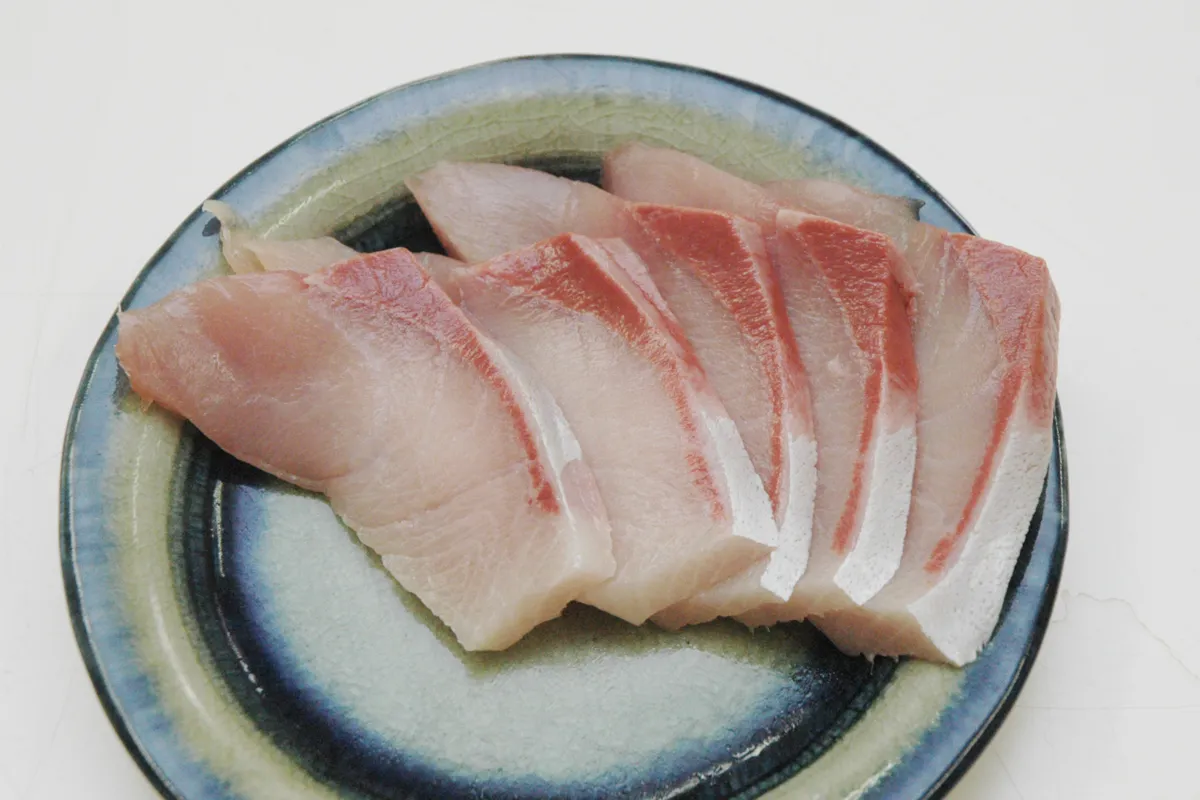 青緑の縁取りの和皿に並べた養殖ブリの厚めの刺身スライス。1切れずつに赤い血合いの筋と白い脂が入り、身は淡いピンク色でツヤがある