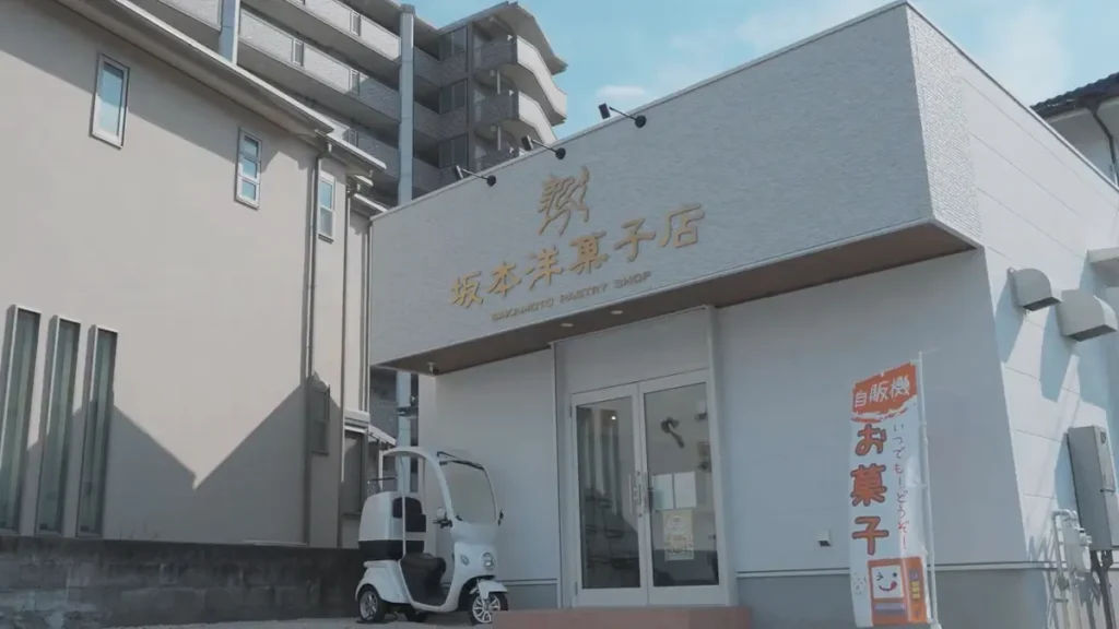 坂本洋菓子店 外観｜白い建物に金色ロゴとお菓子自販機がある洋菓子店