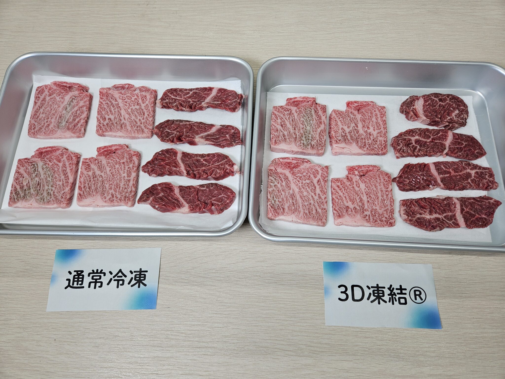 白い紙を敷いた銀色のバットを左右に並べ、淡い赤色で白いサシの入った四角い牛肉と濃い赤色の細長い牛肉を配置し、手前に「通常冷凍」「3D凍結®」の札を置いた凍結前の比較写真