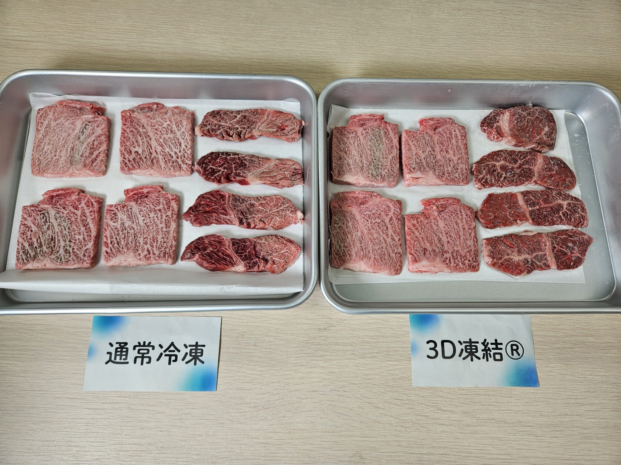 左右の銀色バットに、表面へ霜の付いた淡い霜降り肉と濃い赤色の牛肉を並べ、手前に「通常冷凍」「3D凍結®」の札を置いた凍結後の比較写真