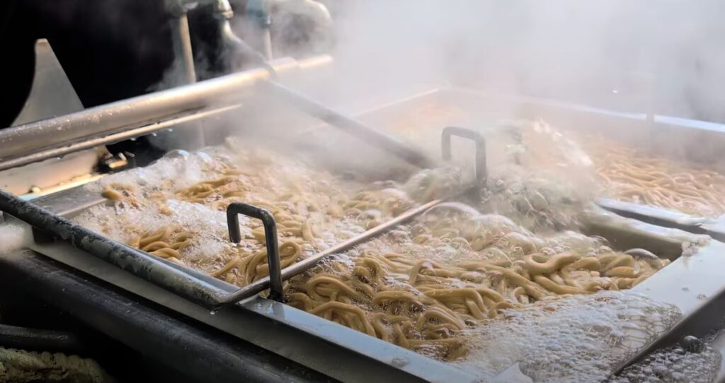 製麺工場で湯切り工程中の麺|山和製麺の製造現場・茹で作業の様子