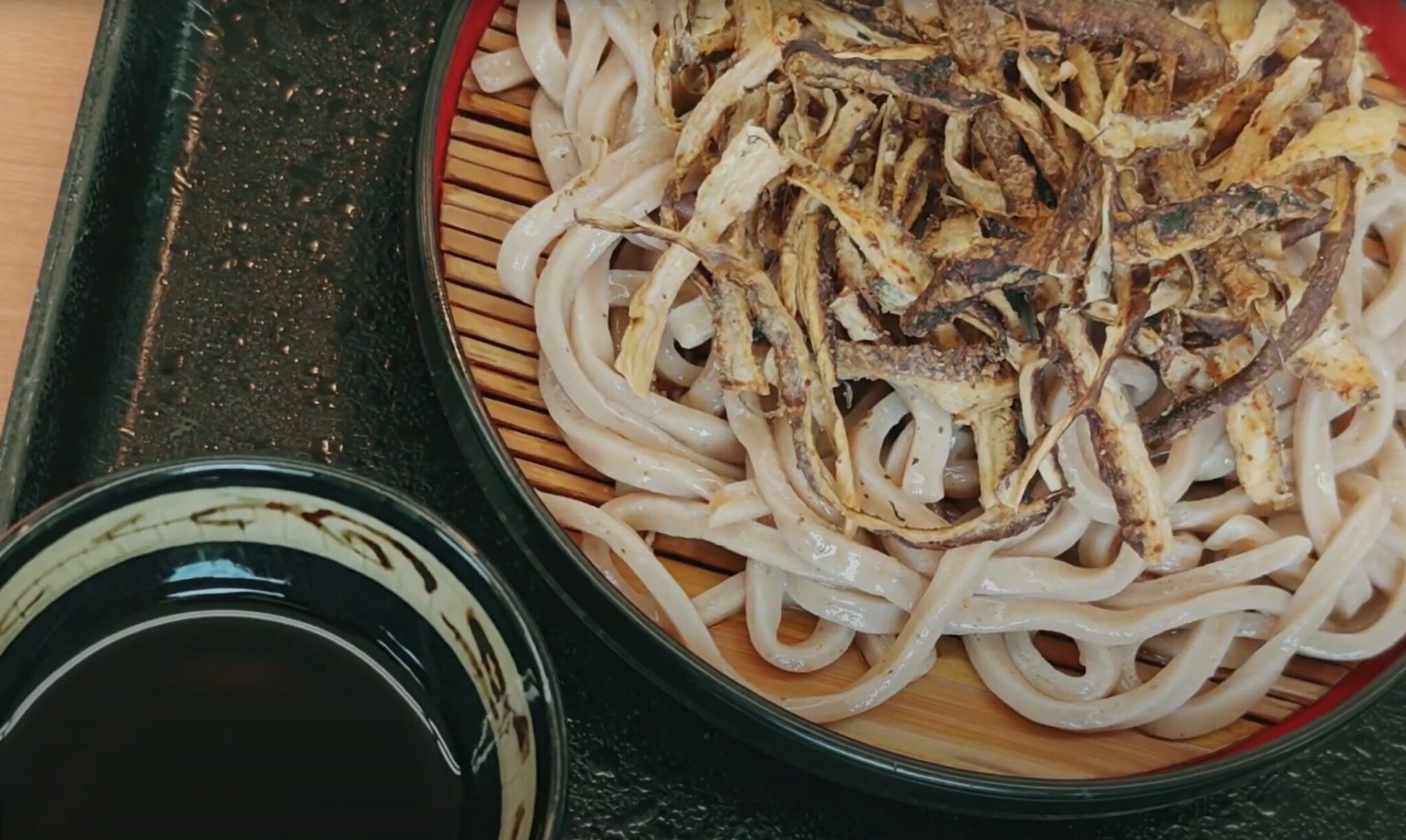 すだれを敷いた器に盛られ、揚げごぼうをのせたざるうどんとつけつゆ