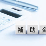 補助金を活用した設備導入や省エネ対策をイメージした写真｜電卓とペンと補助金の文字ブロック