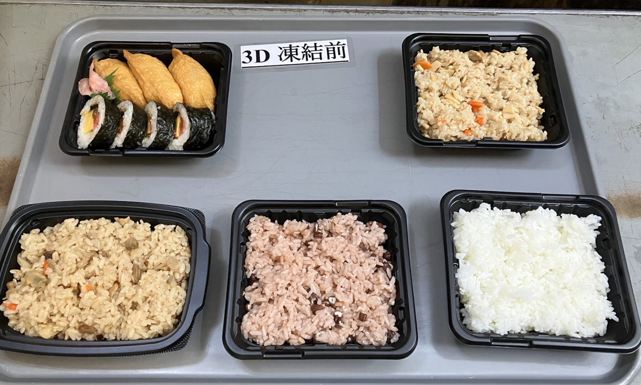 トレイ上の黒い容器に白米、赤飯、鶏飯、炊き込みご飯、いなり寿司と海苔巻きを並べ、中央に「3D凍結前」と表示した写真