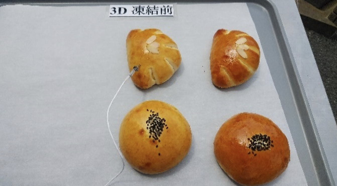 「3D凍結前」の札がある灰色トレーに、黒ごまをのせた丸いパン2個とアーモンドをのせた葉形のパン2個を並べ、左上のパンに温度センサーを差した写真