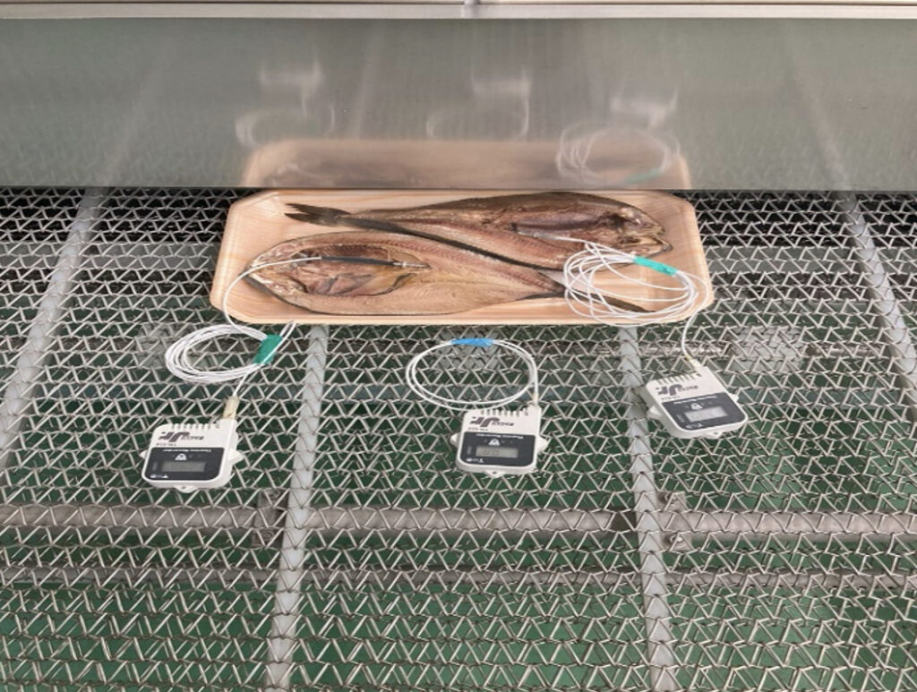 トンネルフリーザーのベルトに載せられたトレイ入りのほっけ（冷凍後）