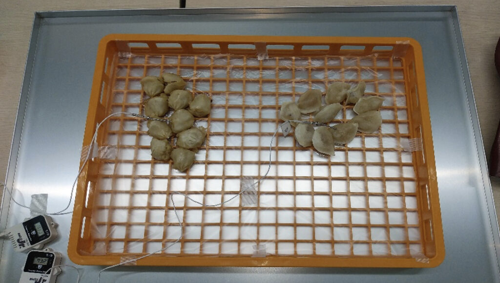 トレーの上に水餃子、小籠包が入った番重が乗せられている（冷凍前）