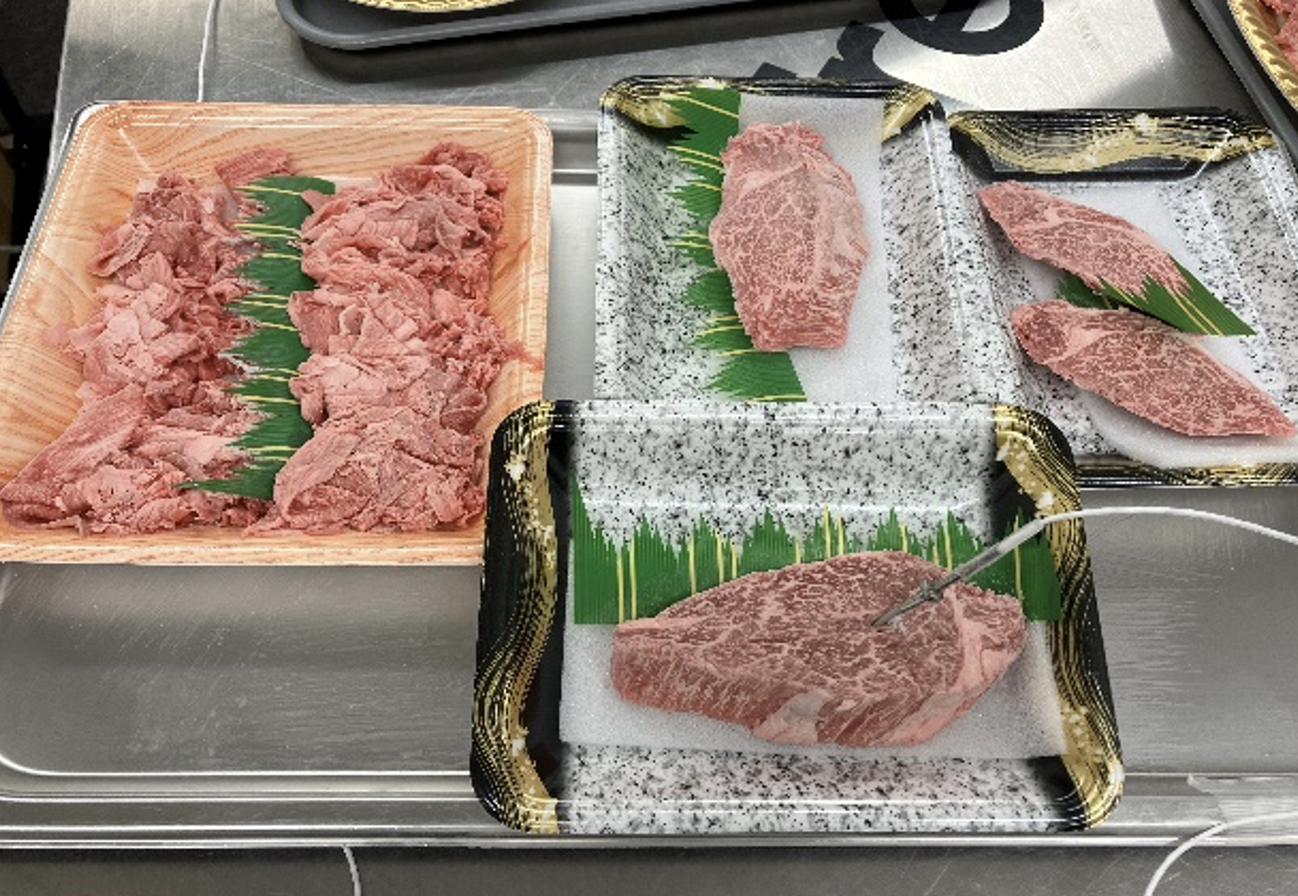 ステンレス台のトレーに並ぶ淡い赤色の牛肉と、手前の霜降り厚切り肉の中心へ差し込まれた温度計のプローブ