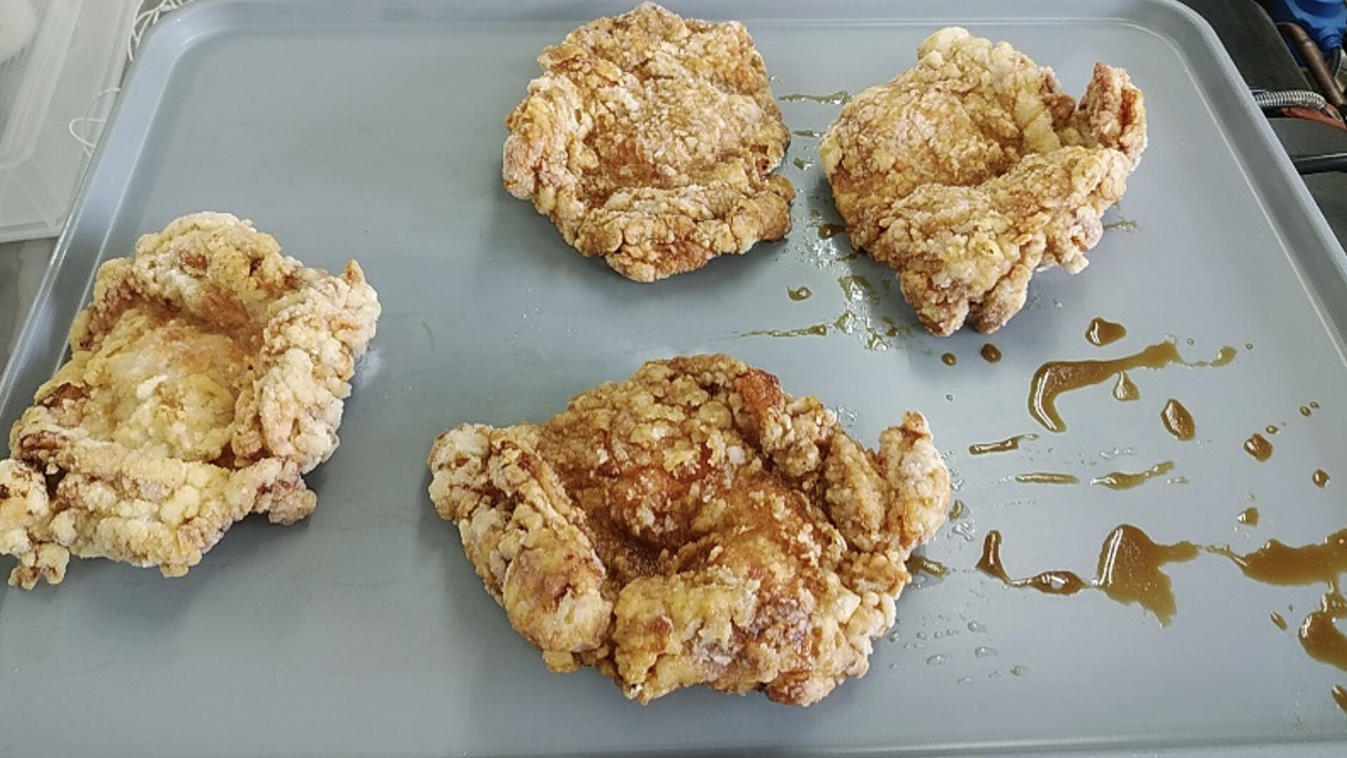 灰色のトレーに衣を付けて揚げた鶏肉を並べ、食品の周囲に褐色の甘酢が流れている投入前の様子
