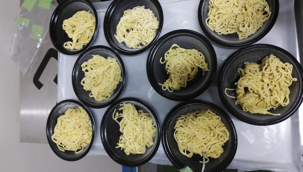 トレーに並べられた容器に入ったたくさんの中華麺が急速冷凍された状態