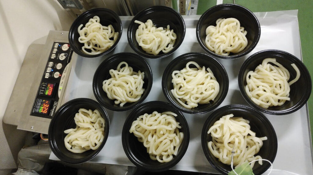 トレーに並べられた容器に入ったたくさんのうどん