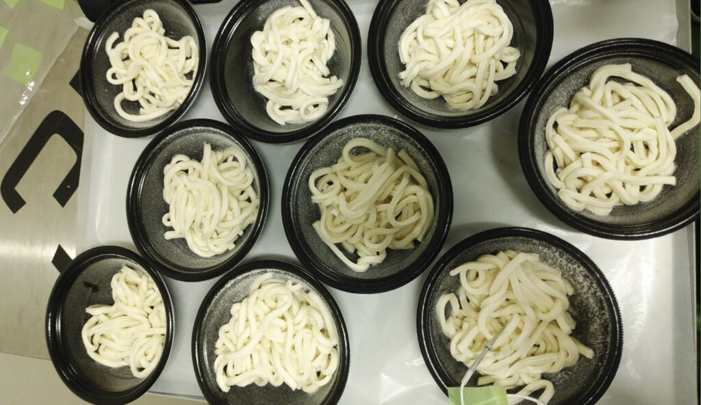 トレーに並べられた容器に入ったたくさんのうどんが急速冷凍された状態