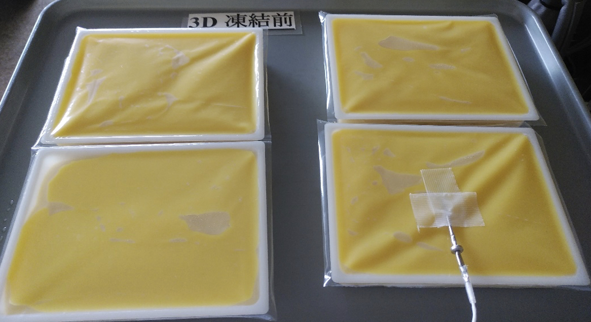 アルミトレーに並べた黄色いごま豆腐入りの四角形容器4個。右下の容器に温度センサーがテープで固定され、奥に「3D 凍結前」の表示がある