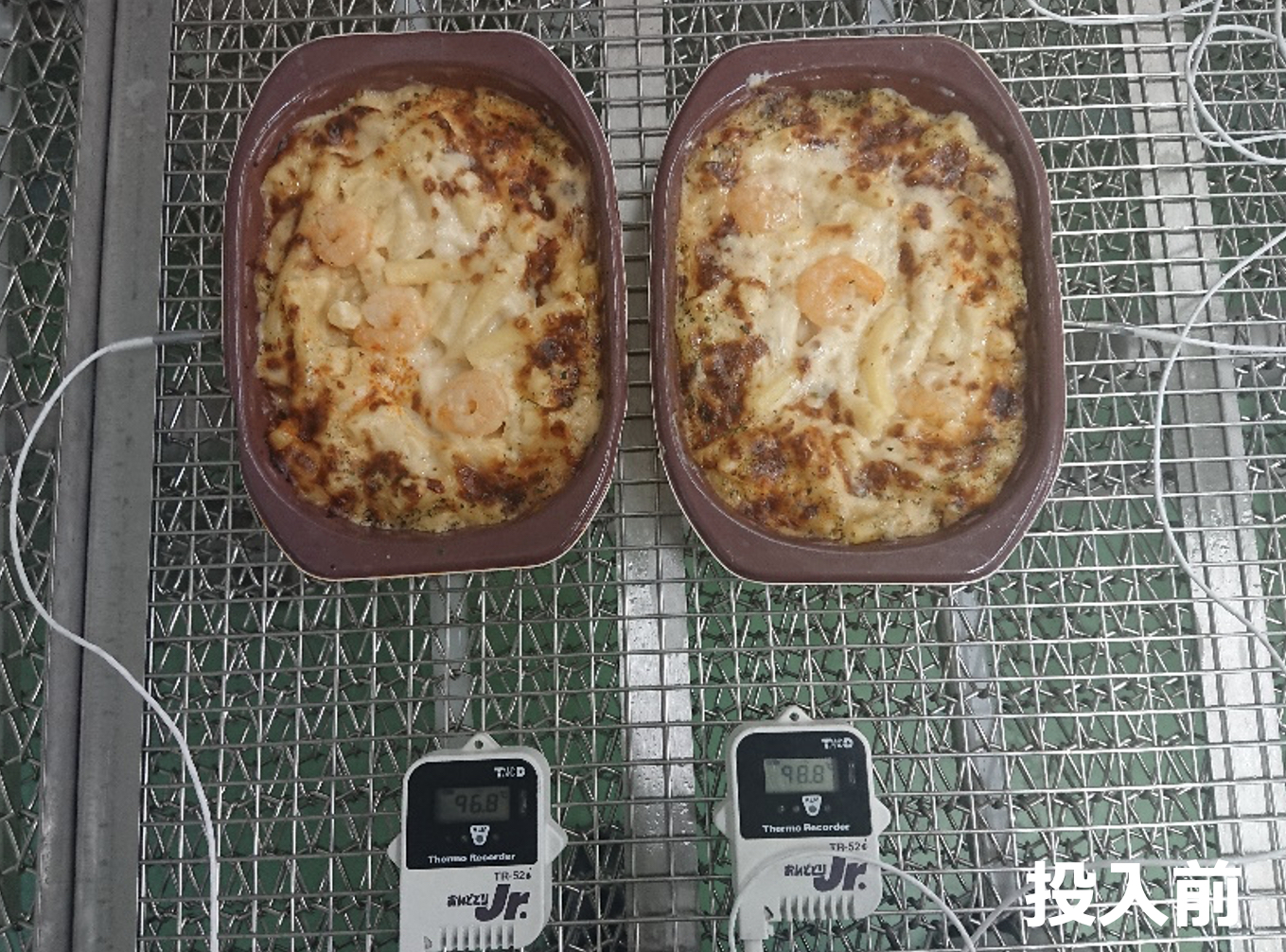 網トレー上に並ぶ茶色い容器2個の焼き色が付いたグラタンと表示付き温度記録計2台、右下に「投入前」と記された写真