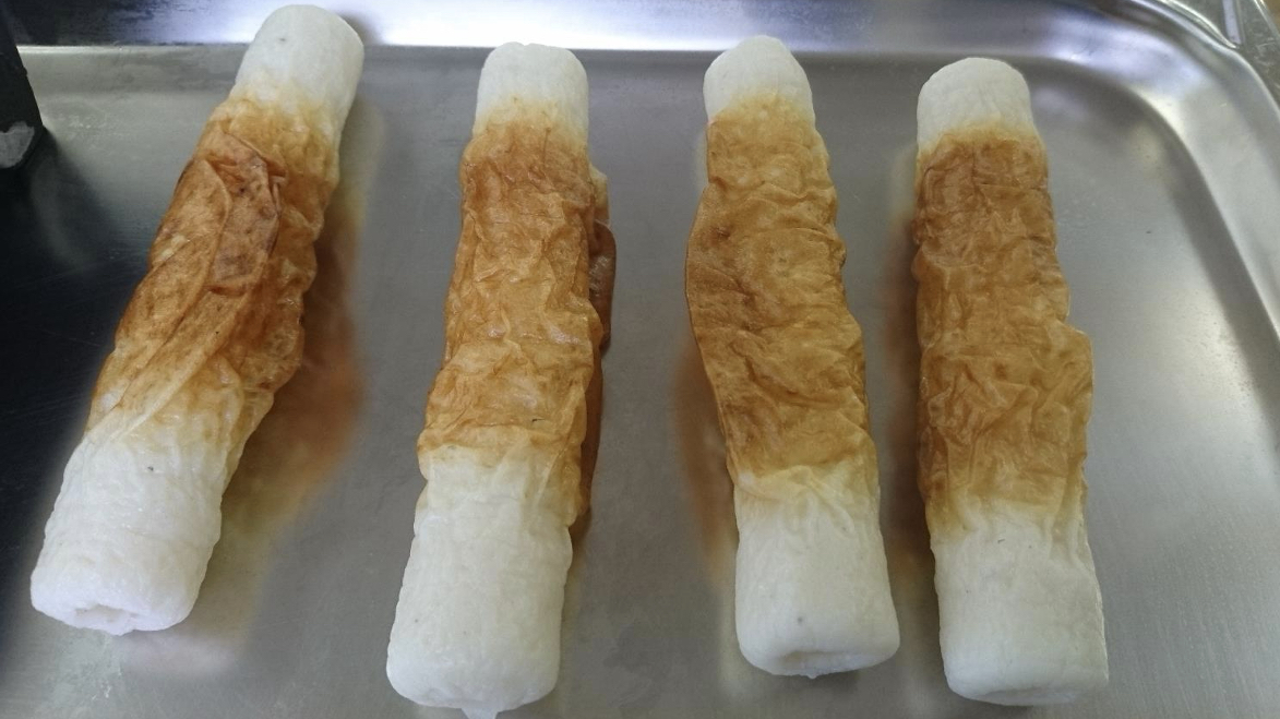 銀色のアルミトレーの上に、中央部が茶色く焼けて両端が白い包装なしの焼きちくわ4本を、間隔を空けて縦向きに並べた写真