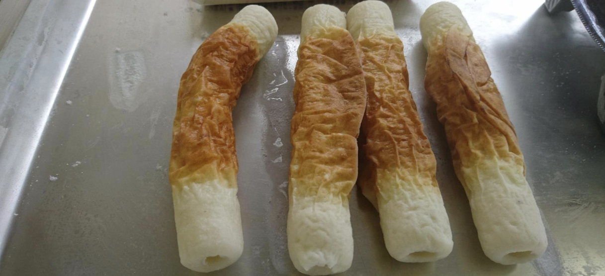 銀色のアルミトレーに、茶色い焼き面と白い端部のある筒状のちくわ4本を奥から手前へ並べ、手前側の穴が見える写真