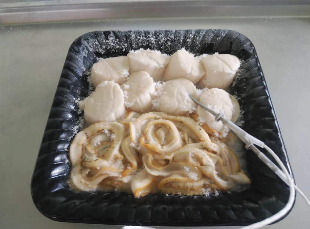 急速冷凍された黒いトレイの中に入った生ホタテ