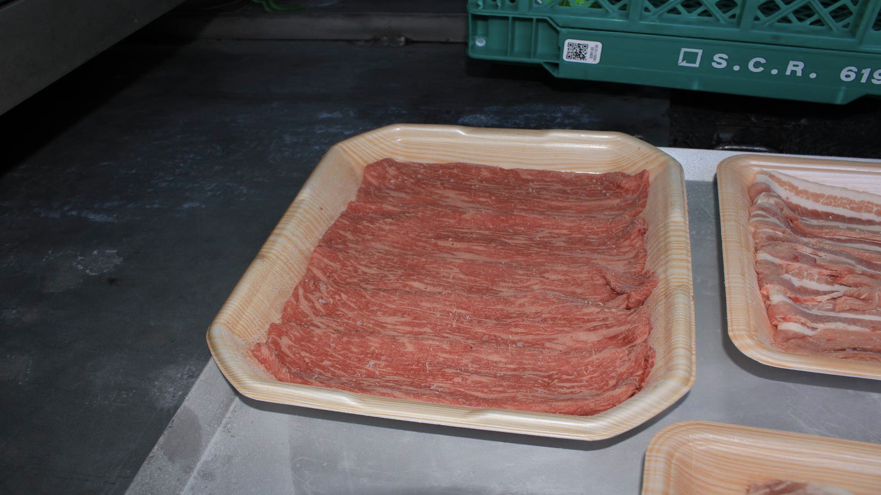 白い台の上のベージュ色トレーに、表面へ白い霜が付いた赤い薄切り牛肉を重ねて並べた様子。右端に別の肉トレーが一部写る